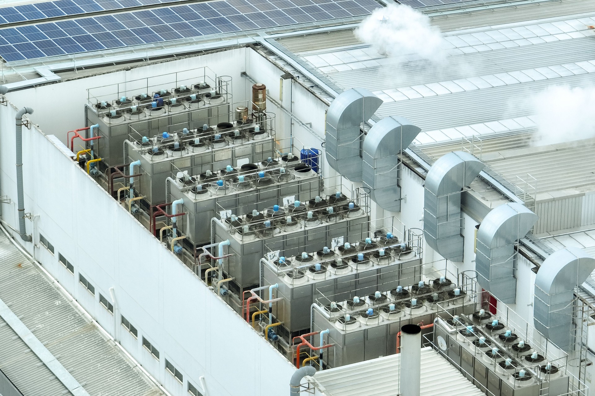 Sustainable industrial rooftop. Aerial view showcasing solar panels, ventilation systems, and industrial chillers. Renewable energy and efficient cooling in modern manufacturing facilities.